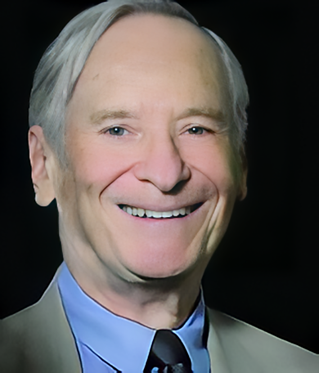 A headshot of Charlie L. Reinhart. He is an older man with greying hair and wearing a grey suit and blue shirt.