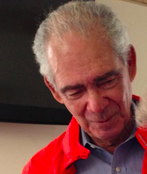 Headshot of Carlos Cuevas. He is a man with greying hair wearing a red jacket and a grey shirt.