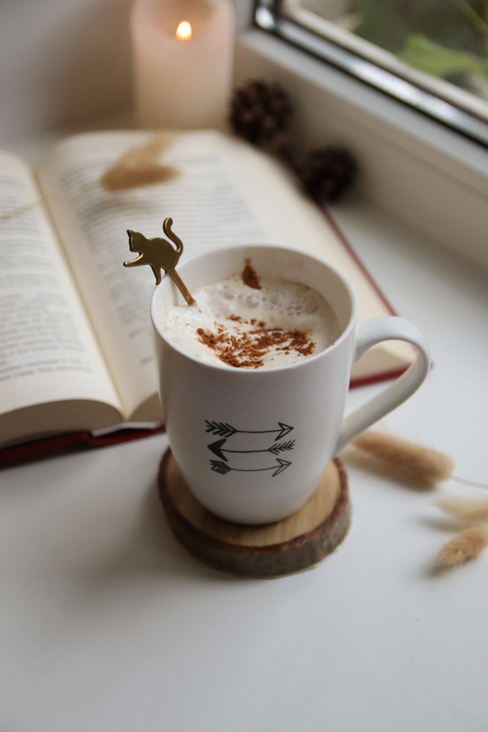 a cup of coffee in a white mug with a book and candle in the background.