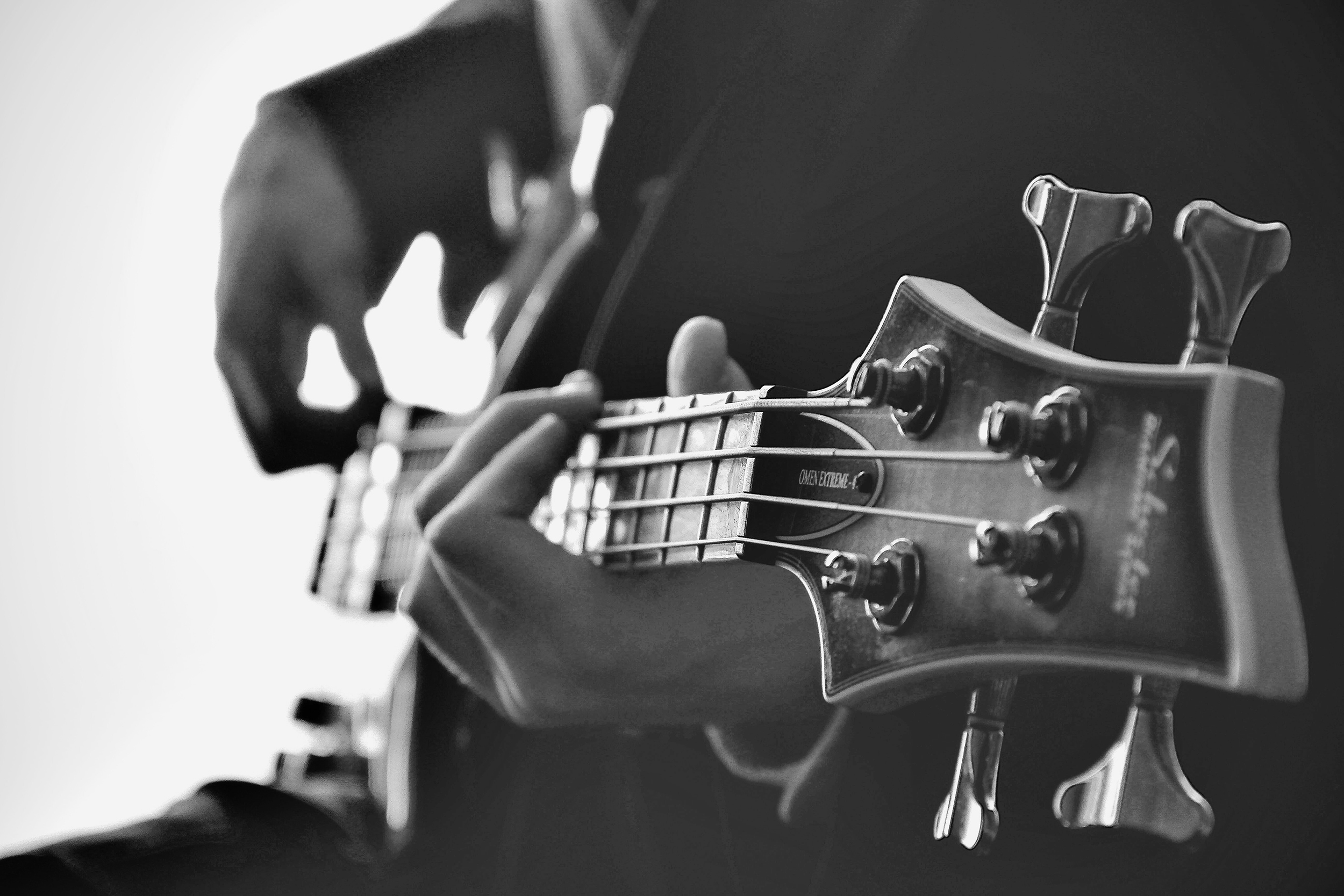 A black and white photo of a person in a suit playing a guitar, showing their hands on the strings and frets. 