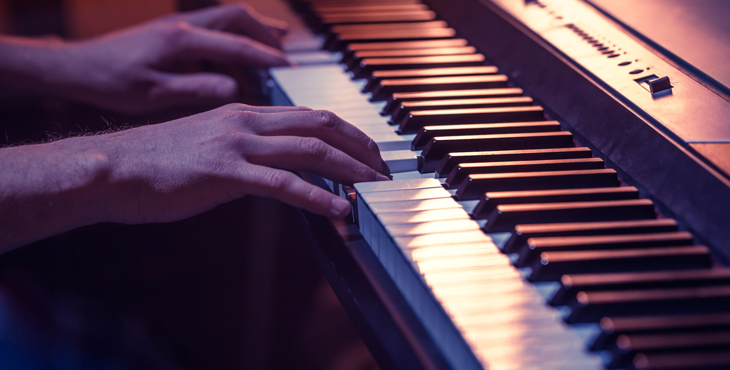 A color photo of light skinned male hands on a piano keyboard.