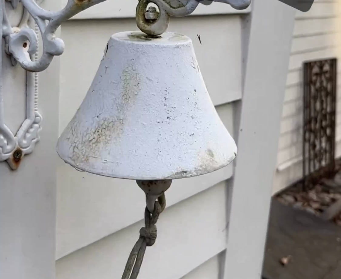 A white bell hanging outside a door predating modern door bells.