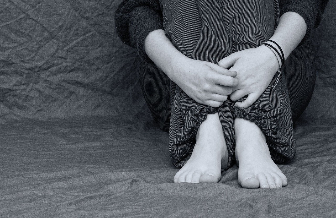 Picture in black and white of person's hands and arms wrapped around legs in a crouched position. The picture is from the shoulders down. 